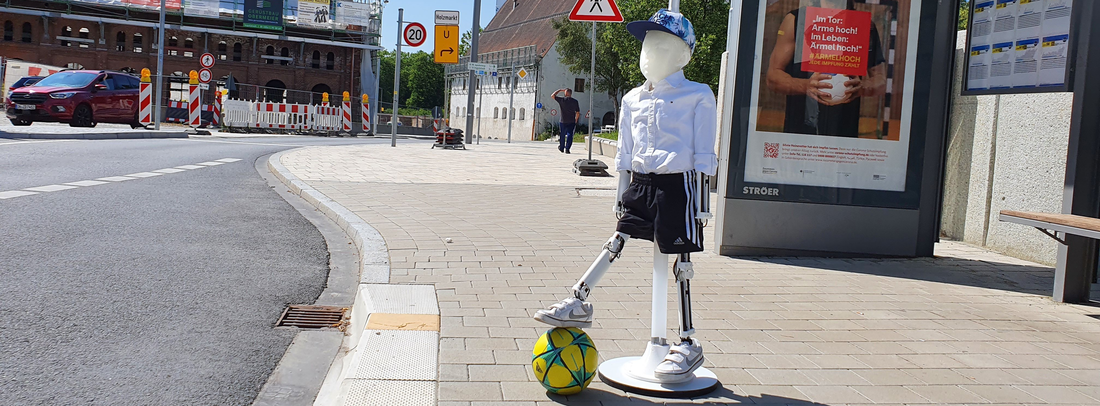 Illustration of the child dummy with a ball on its foot by a street