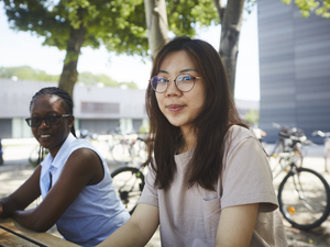 Zwei Studentinnen auf Sitzgelegenheit vor Gebäude G