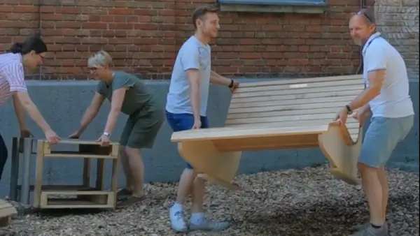 [Translate to English:] Zwei Männer tragen eine Holzliege, zwei Frauen platzieren einen aus Palettenholz gebauten Tisch