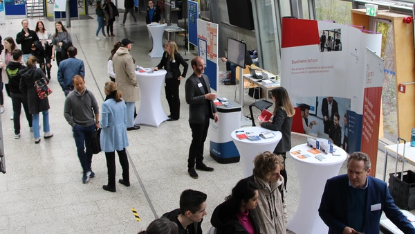 Menschen in einem Foyer und am Messestand